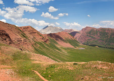 Green pastures rise up to red mountain peaks