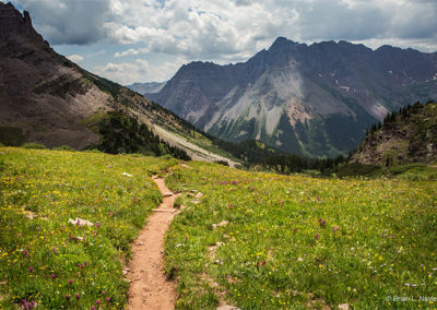 The descent through alpine flora leads to new mountain scenes.